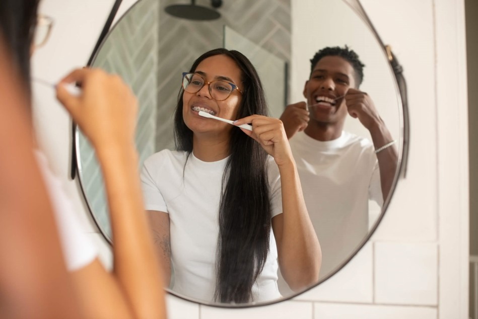 Two people brush and floss in the mirror
