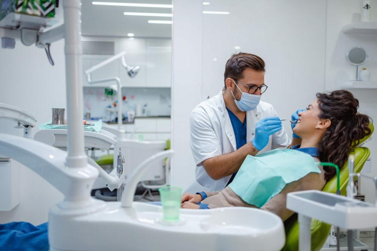 A person in a white coat and blue gloves examining a person's teeth